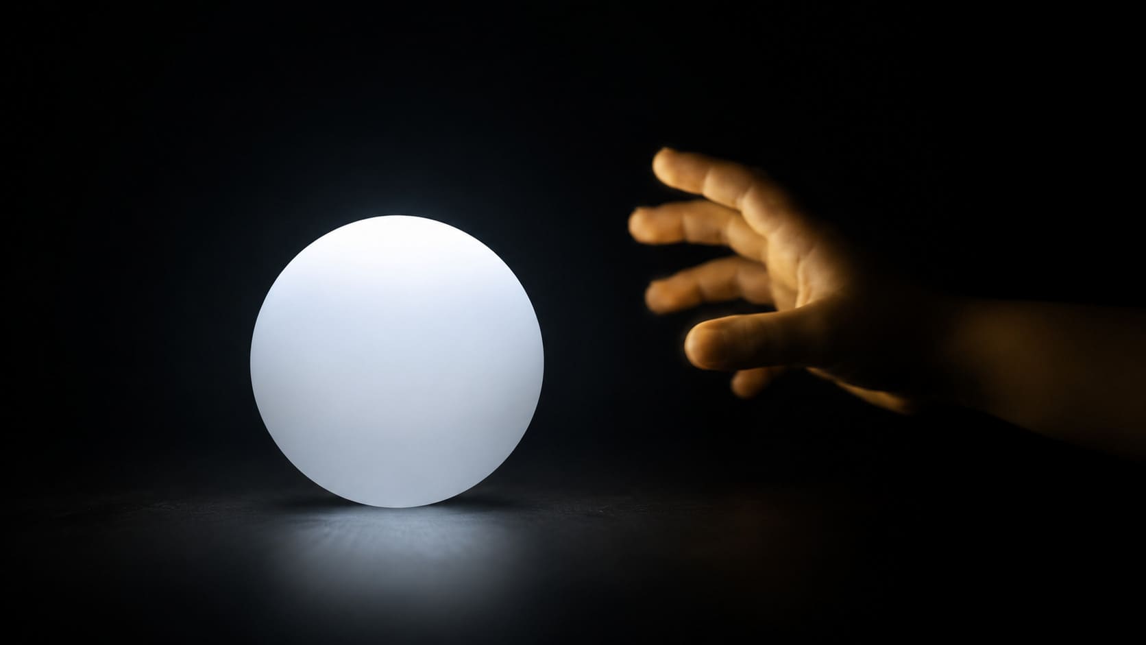 A perfectly smooth, cold-white geometric sphere in a stark charcoal void, with a child's hand illuminated by warm amber light reaching toward it