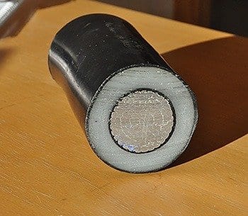 A high-voltage cable cross-section. The electrically conductive core is covered by a black protective layer, a white insulation layer of plastic and an additional black protective layer. 