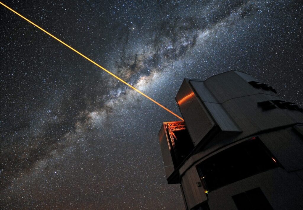 A glowing laser shines forth from the European Southern Observatory’s Very Large Telescope. Piercing the dark Chilean skies, its mission is to help astronomers explore the far reaches of the cosmos. ESO Photo Ambassador Gerhard Hüdepohl was on hand to capture the moment in a stunning portrait of modern science in action.  We have all gazed up at the night sky and seen the stars gently twinkle as the Earth’s turbulent atmosphere causes their light to shimmer. This is undoubtedly a beautiful sight, but it causes problems for astronomers, who want the crispest possible views. To help them achieve this, professional stargazers use something that sounds as though it has come from science fiction: a laser guide star that creates an artificial star 90 km above the surface of the Earth. The method by which it achieves this is nothing short of remarkable. The laser energises sodium atoms high in the Earth’s mesosphere, causing them to glow and creating a bright dot that to observers on the ground appears to be a man-made star. Observations of how this “star” twinkles are fed into the Very Large Telescope’s adaptive optics system, controlling a deformable mirror in the telescope to restore the image of the star to a sharp point. By doing this, the system also compensates for the distorting effect of the atmosphere in the region around the artificial star. The end result is an exceptionally crisp view of the sky, allowing ESO astronomers to make stunning observations of the Universe, almost as though the VLT were above the atmosphere in space. Links Adaptive Optics and the Laser Guide Star: http://www.eso.org/public/teles-instr/technology/adaptive_optics.html ESO Photo Ambassadors