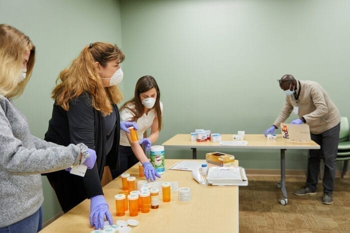 Julia Schweiger (black shirt), lab manager in Eric Lenze’s lab, organizes packets for a COVID-19 trial with the help of professional rater Leonard Imbula, and her daughters, research coordinator Abigail Schweiger (white shirt) and Nadia Schweiger (grey shirt) at the Taylor Avenue Building on April 9, 2020. MATT MILLER/WASHINGTON UNIVERSITY SCHOOL OF MEDICINE