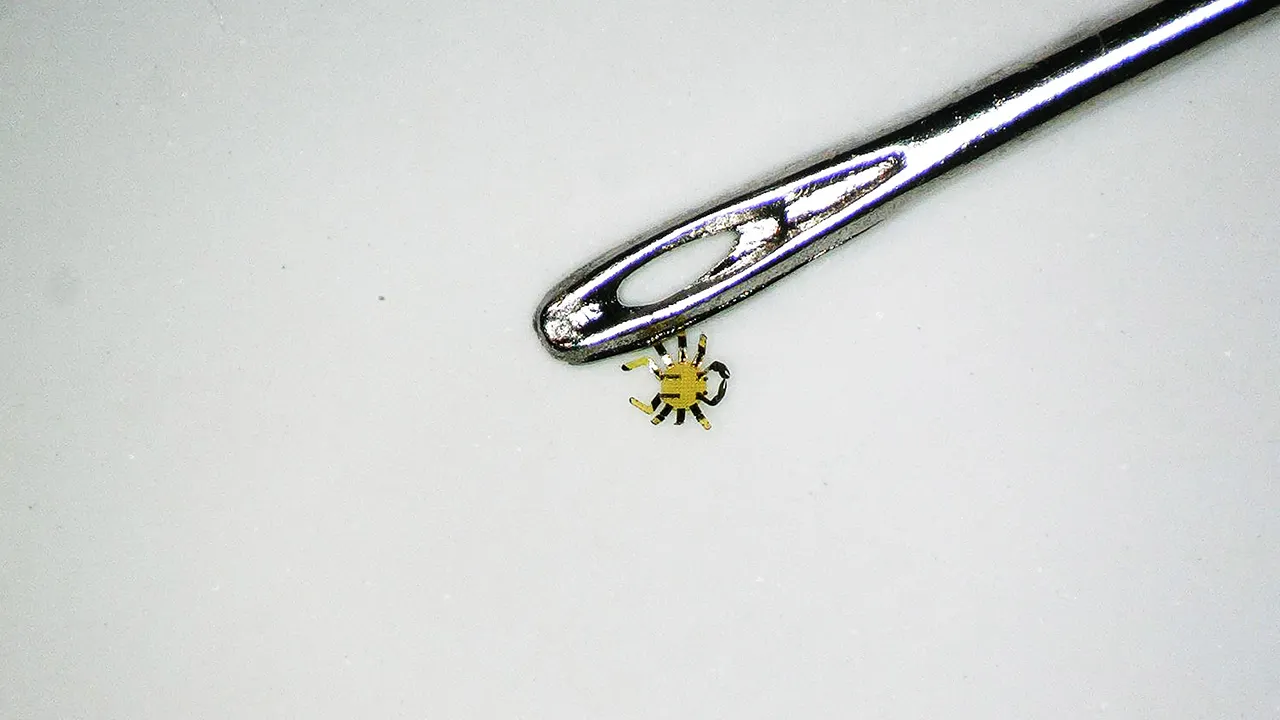 Smaller than a flea, tiny robotic crab sits next to the eye of a sewing needle.