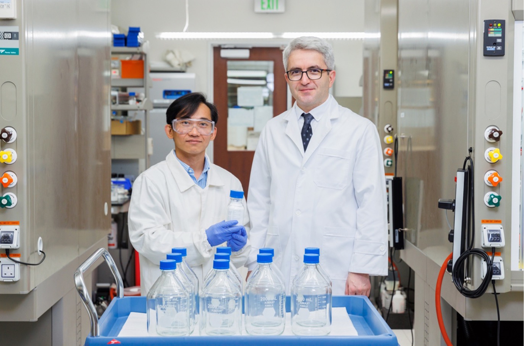 Dr. Thien Nguyen (left) and Professor Cafer T. Yavuz (right) pose with a bottle of CO2-loaded guanidinium sulfate salt (held by Dr. Nguyen). The ten gas-filled, two-liter bottles in front represent the required space for the same amount of carbon dioxide that would be needed were it not being held in clathrate form (small bottle). Photo: KAUST